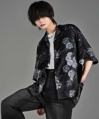 Male model wearing a black loose men's shirt with a floral print against a gray background.
