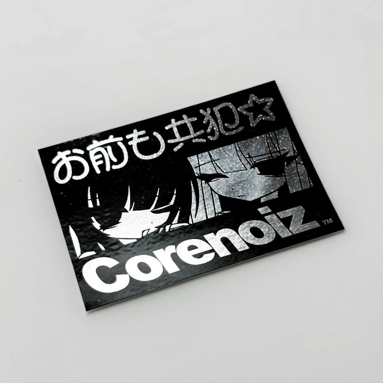 Rectangular black mini sticker on a white background showing Japanese text at the top, two stylized faces in the center, and large Latin-script text along the bottom.