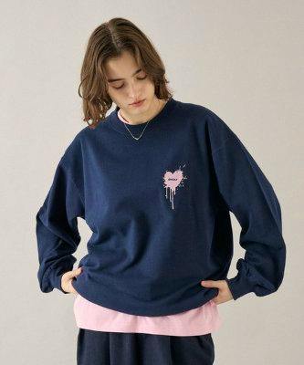 Model wearing a navy cotton sweatshirt with a small pink heart logo on the left chest, layered over a pink shirt.