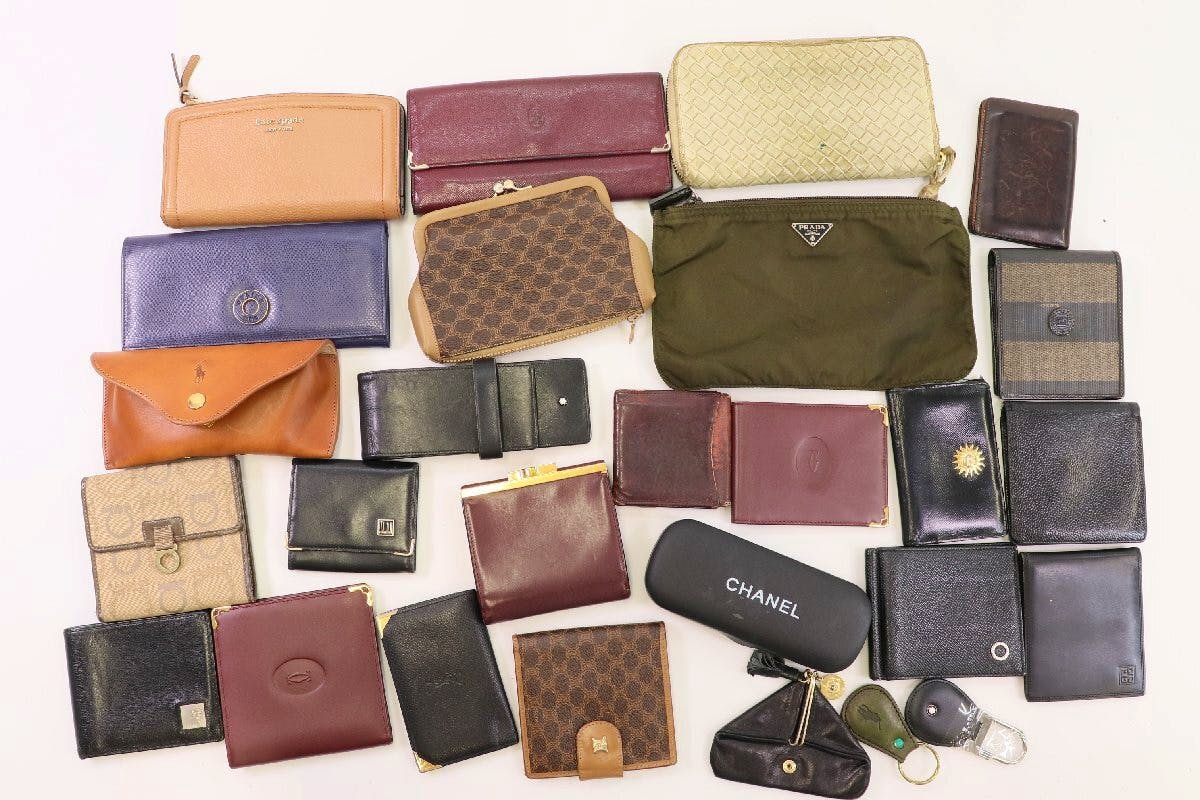 Top-down photo of assorted wallets, eyeglass cases, keyrings, and small fashion accessories arranged on a white background.