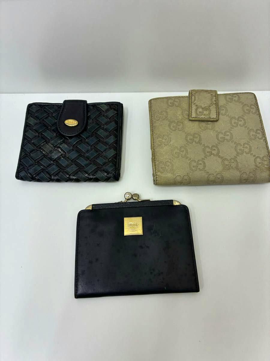 Three wallets on a white surface: a black woven Bally wallet, a beige Gucci GG canvas wallet, and a black Céline clasp wallet.
