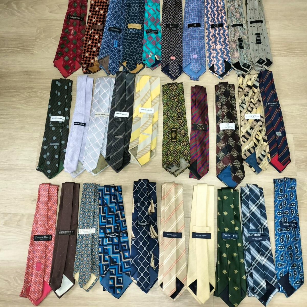 Multiple neckties laid flat in rows on a light wood floor showing various patterns and designer labels.
