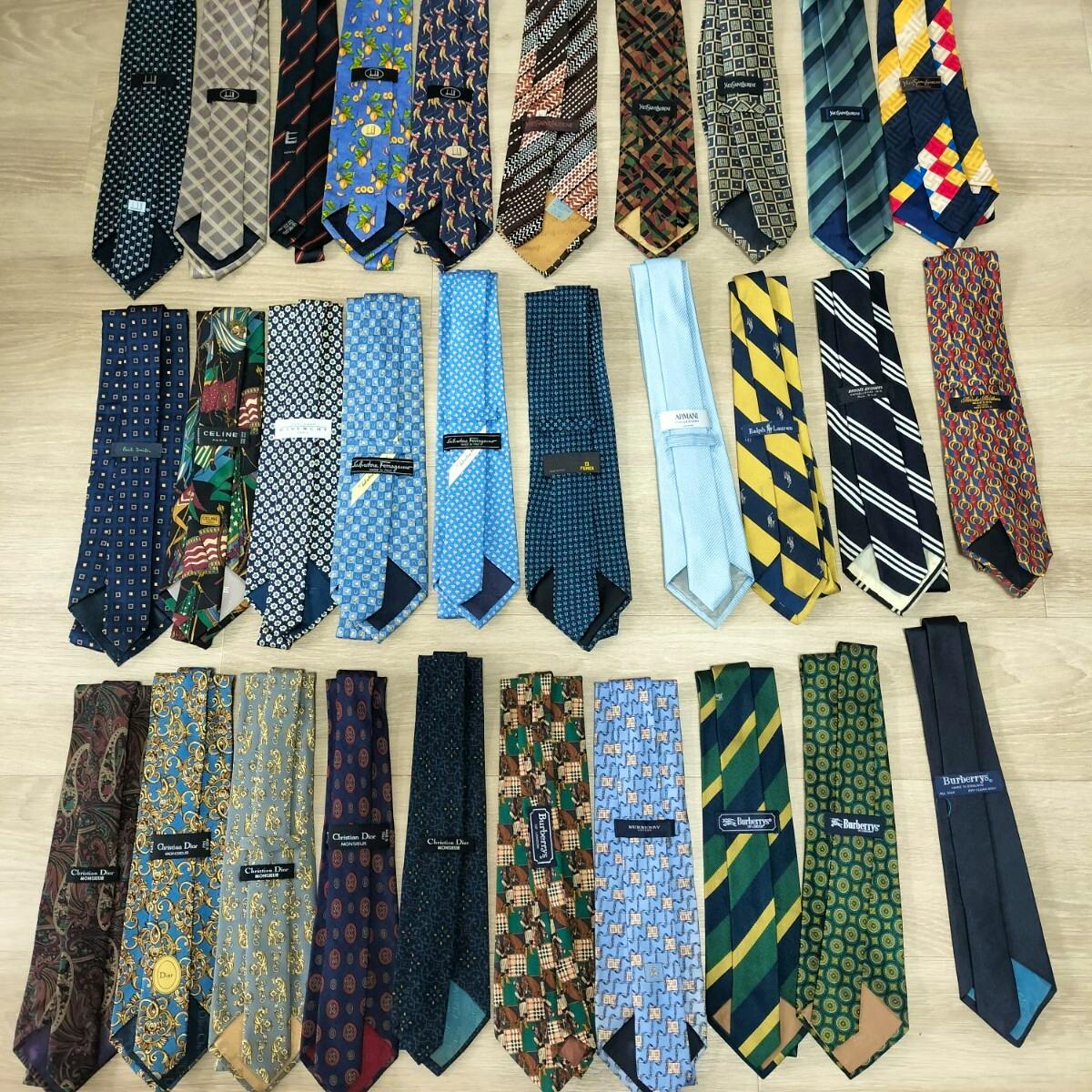Multiple silk neckties arranged in rows on a wooden floor, showing various patterns and visible brand labels.