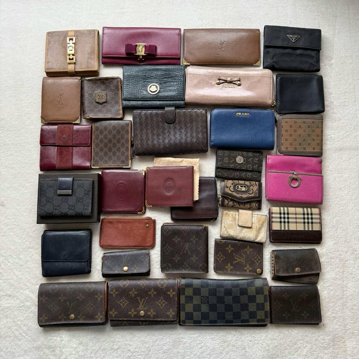 Thirty-three used designer wallets and small leather goods arranged flat on a light fabric background.