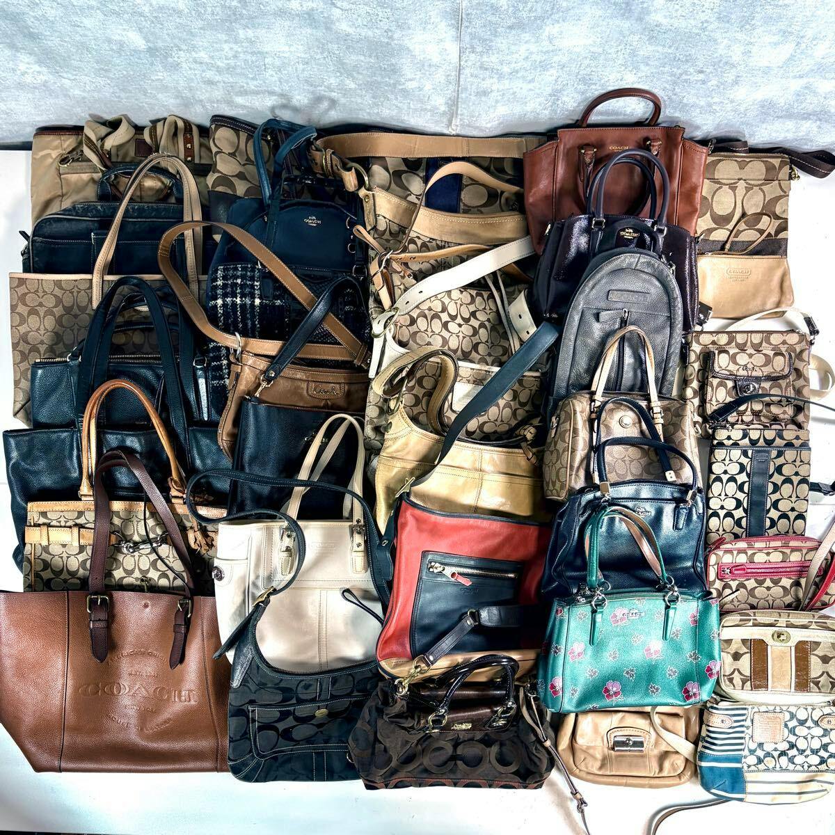 A bulk set of Coach handbags and shoulder bags laid out together showing various signature patterns and colors.