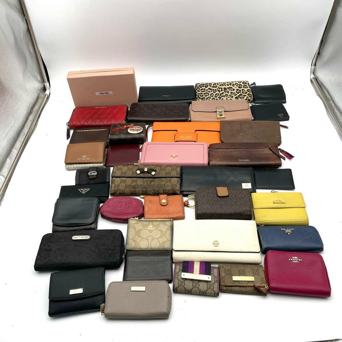 A flat lay photo of many branded wallets and small leather goods arranged on a white background, including visible Gucci pieces.