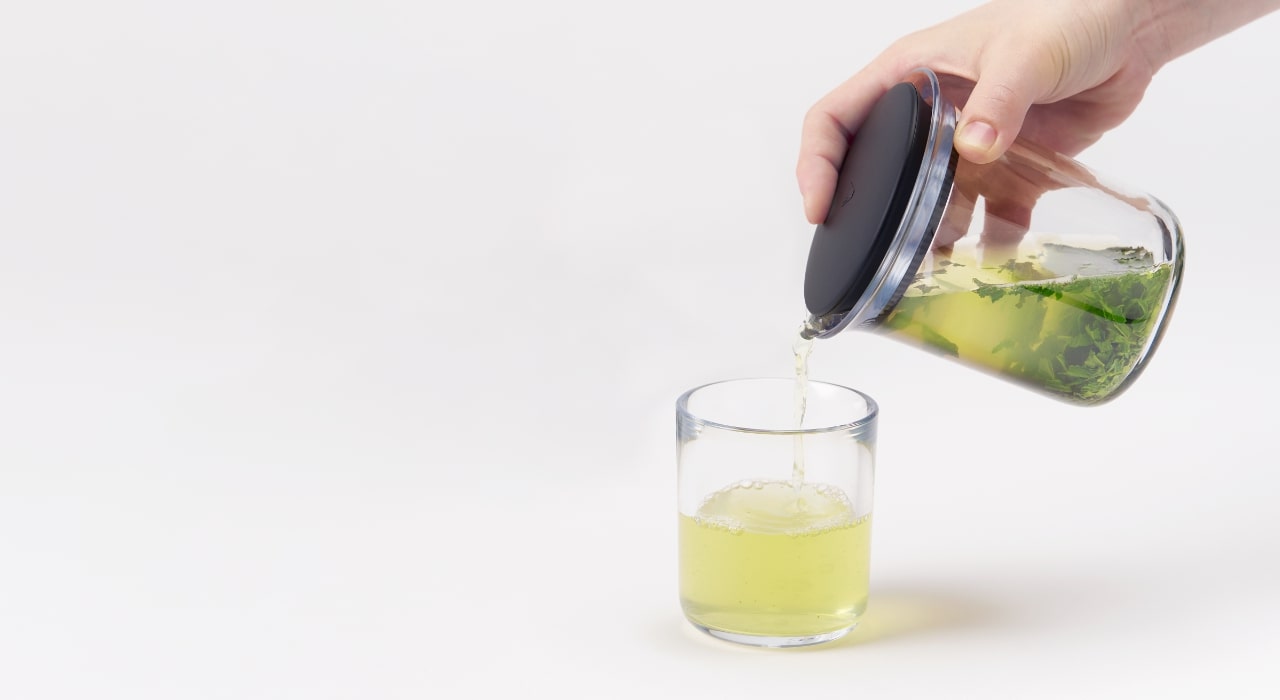 A hand pours tea from the glass 360KYUSU teapot into a clear glass cup.