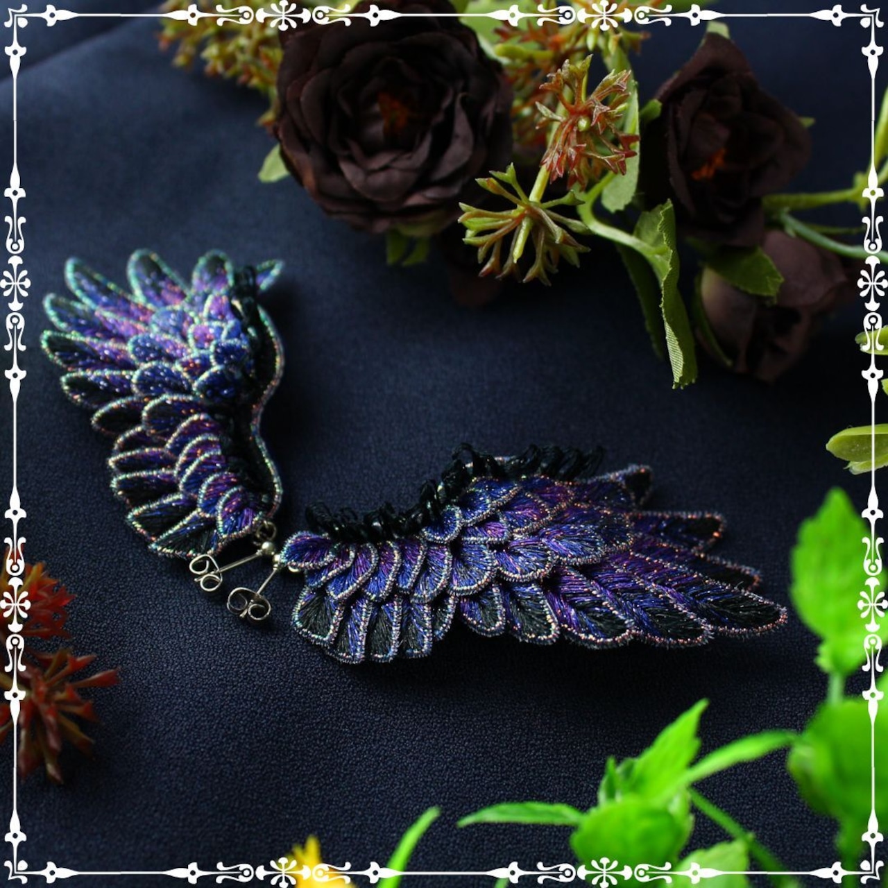 Pair of purple embroidered wing-shaped earrings displayed on dark fabric with decorative flowers.