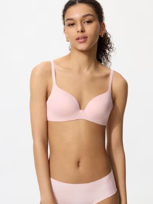 A model wearing a light pink wireless bra and matching underwear against a white background.
