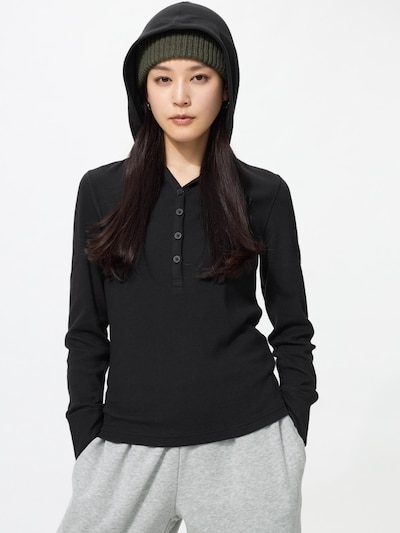 Front view of a model wearing a black ribbed merino-blend polo sweater with a hood and button placket.