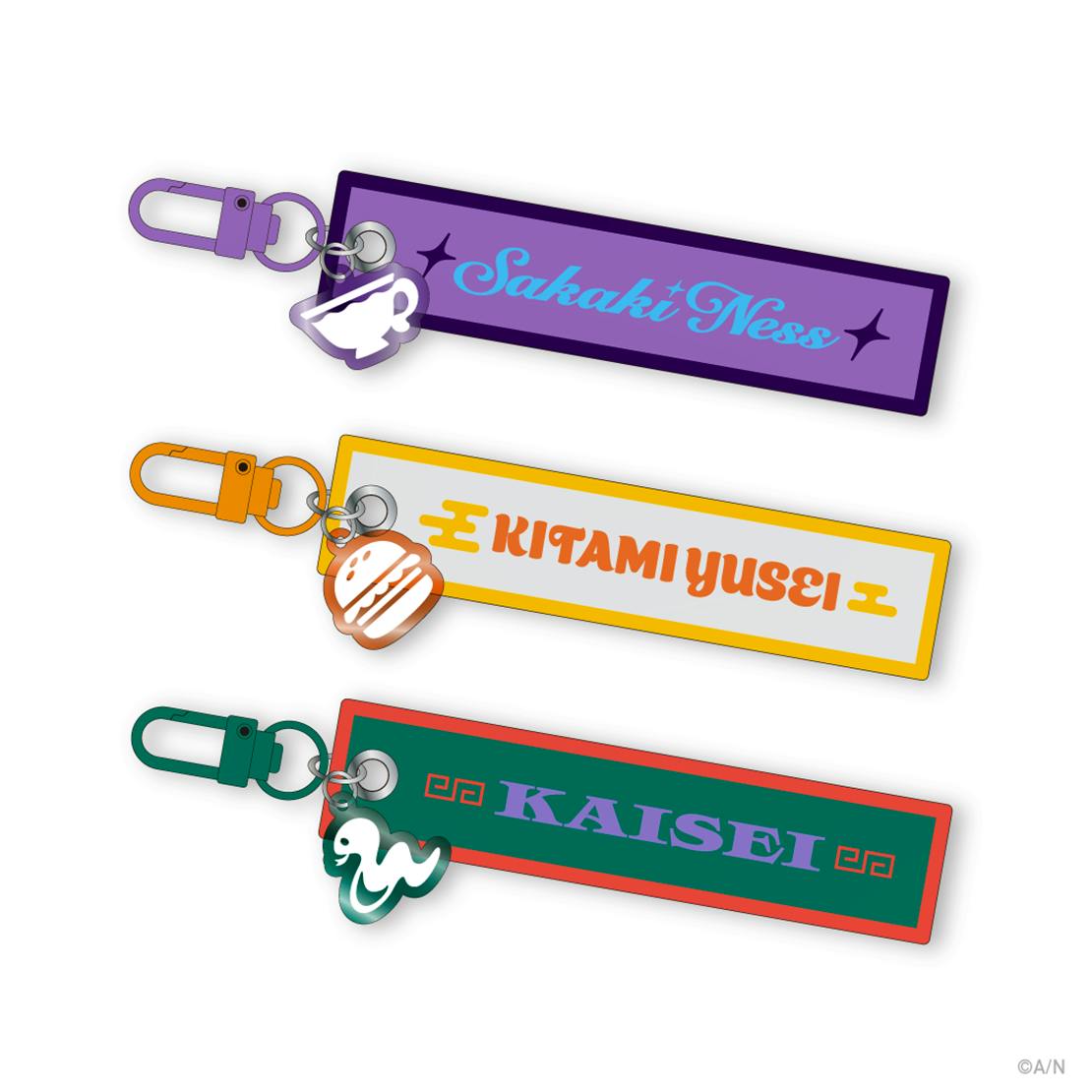 Illustration of three rectangular acrylic name keychains with colored borders and small attached charms, showing the names Sakaki Ness, KITAMI YUSEI, and KAISEI.