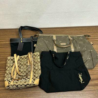Four bags from the lot, including a Coach monogram bucket bag and a black Yves Saint Laurent tote, arranged on a wooden floor.