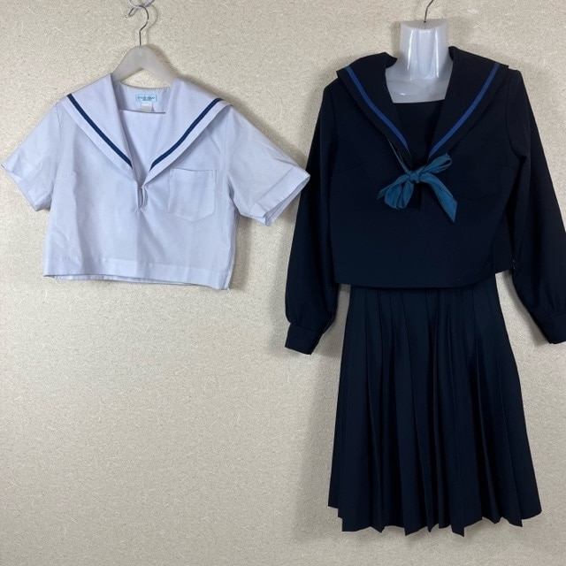 A navy long-sleeve sailor-style school uniform top with matching pleated skirt and a white short-sleeve sailor blouse hanging on hangers.