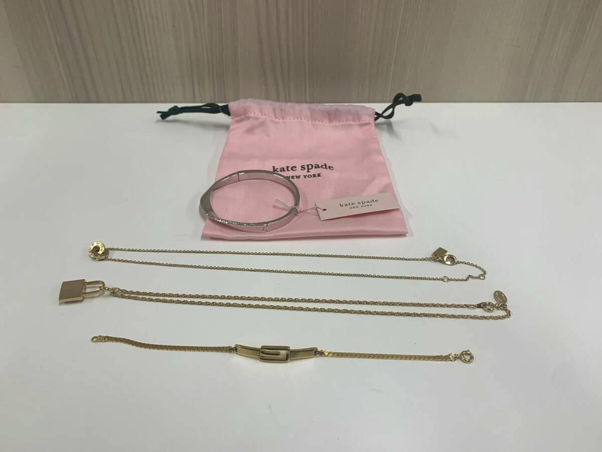 Four jewelry pieces (necklaces/bracelets) and a bangle arranged on a white surface with a pink kate spade pouch.