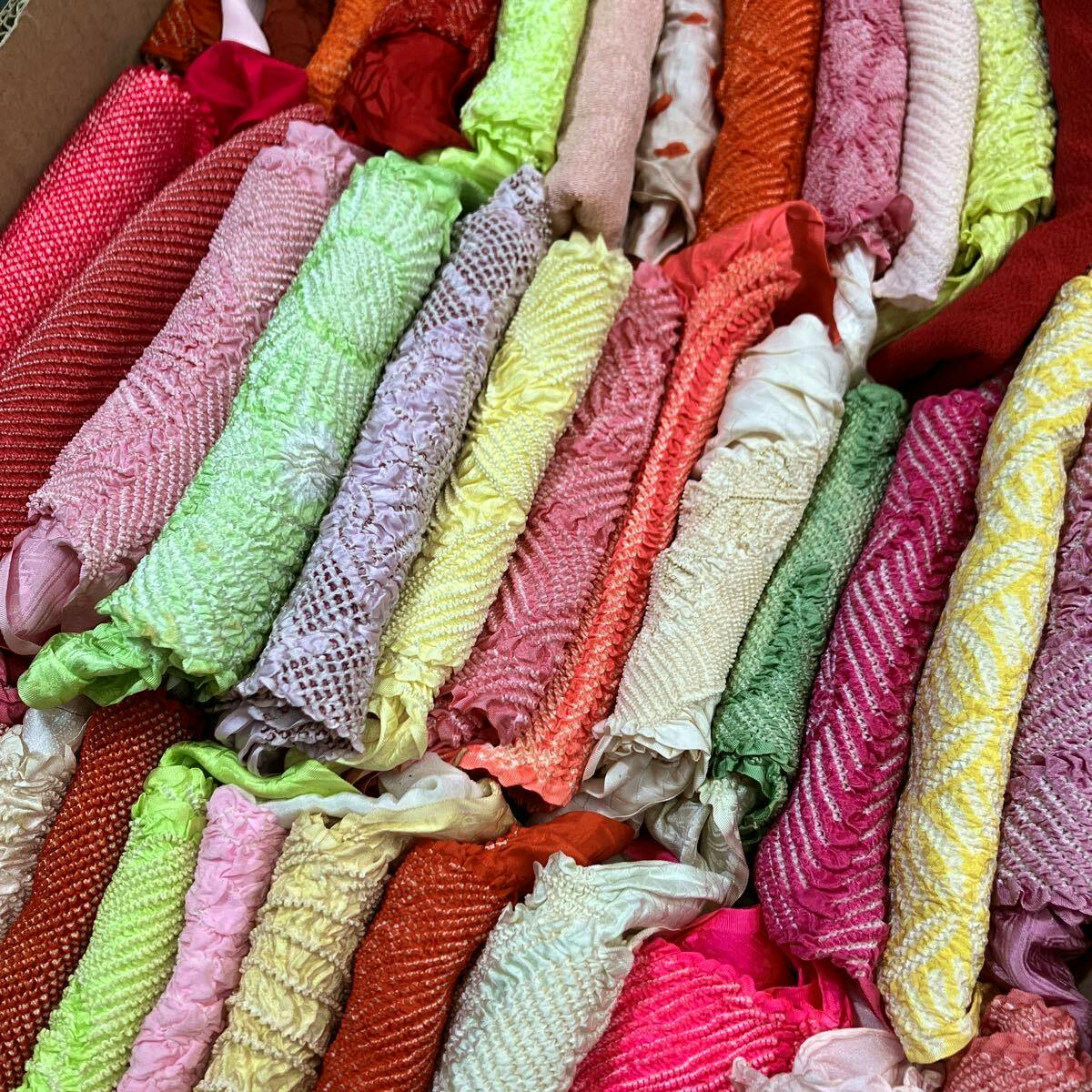 Rolled colorful obiage (kimono sash accessories) with various shibori textures arranged closely in a box.