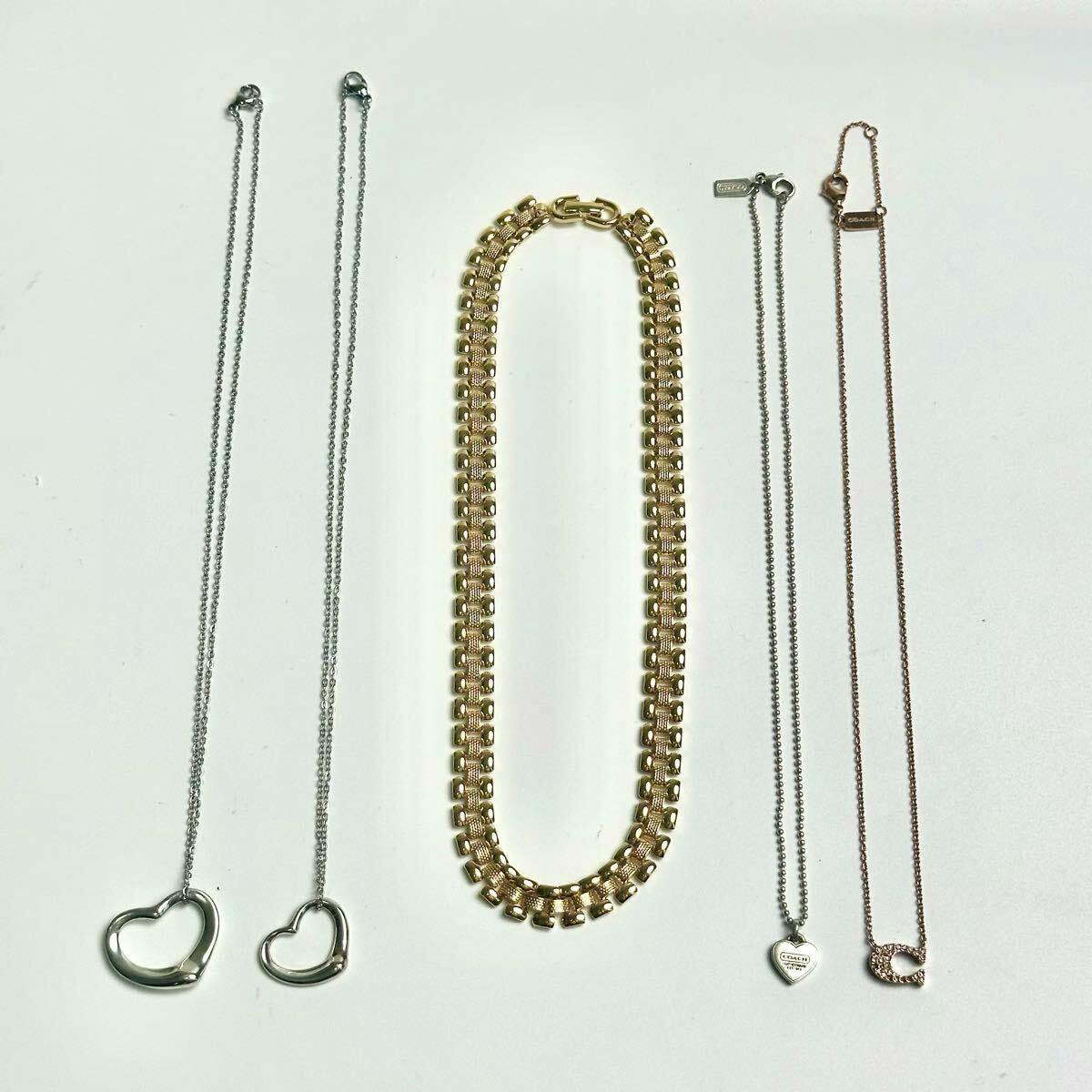 Five necklaces laid flat on a white background: two open-heart pendant chains at left, a wide gold chain in the center, and two thin chains with small charms at right.