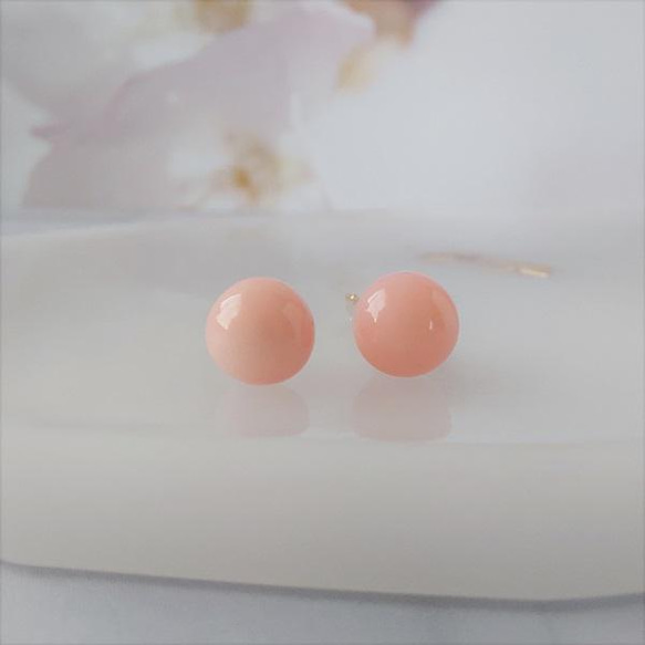 Close-up of a pair of 5mm natural pink coral round bead non-pierced earrings placed on a white surface.