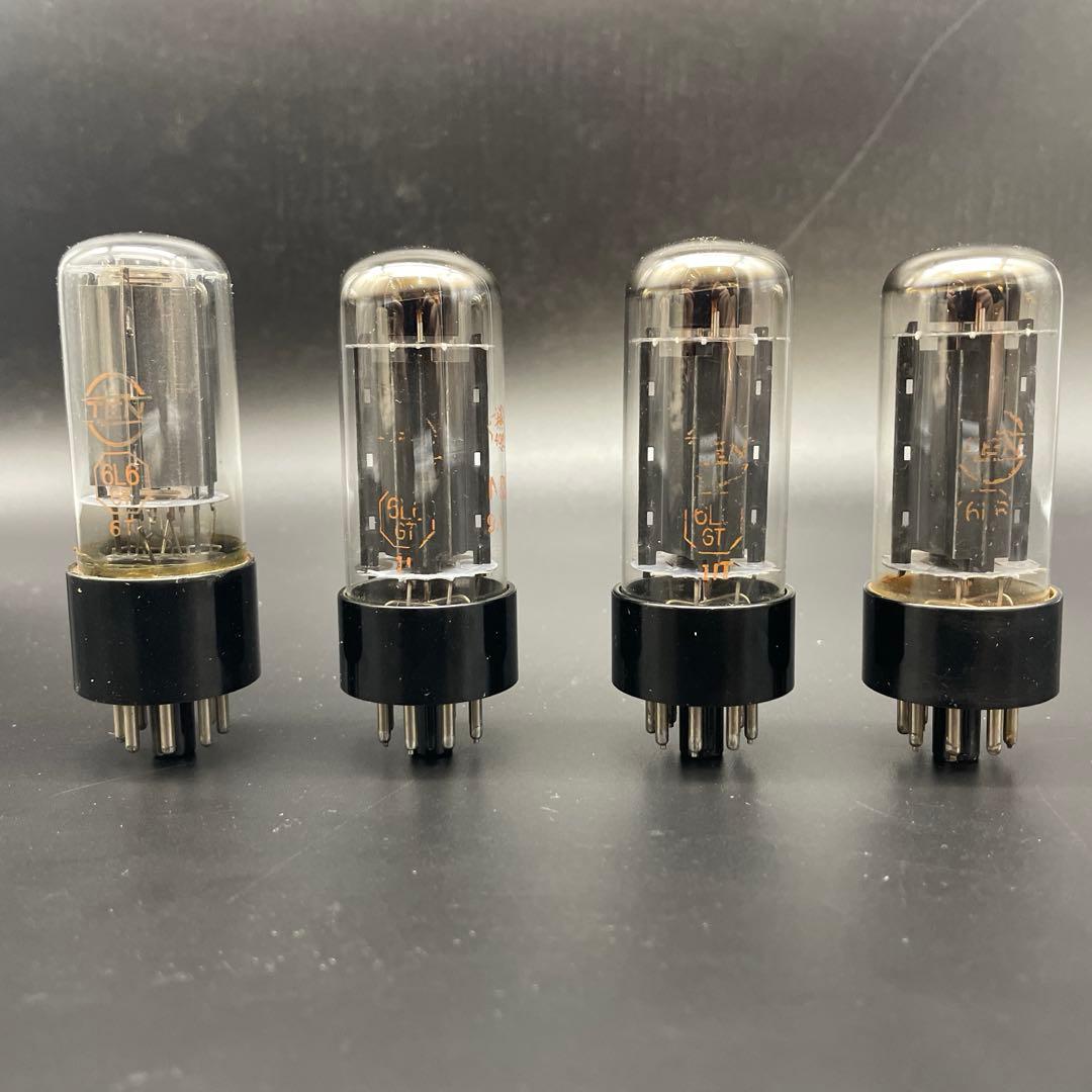 Four 6L6GT vacuum tubes with black bases standing in a row against a dark background.