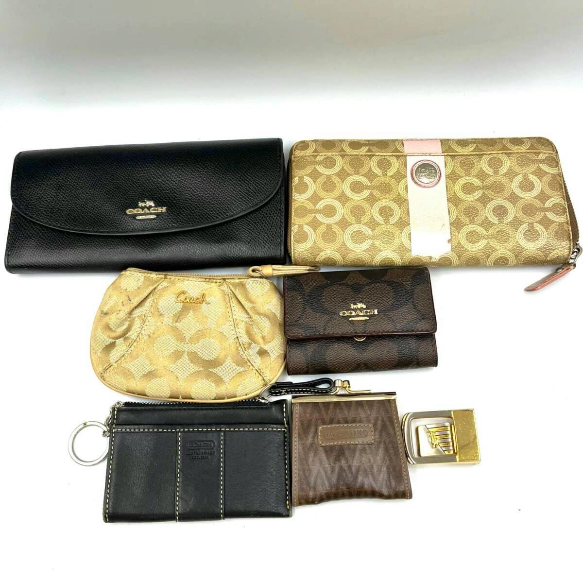 Seven small leather accessories including multiple Coach wallets, coin pouch, key case, and a gold-toned belt buckle arranged on a white background.