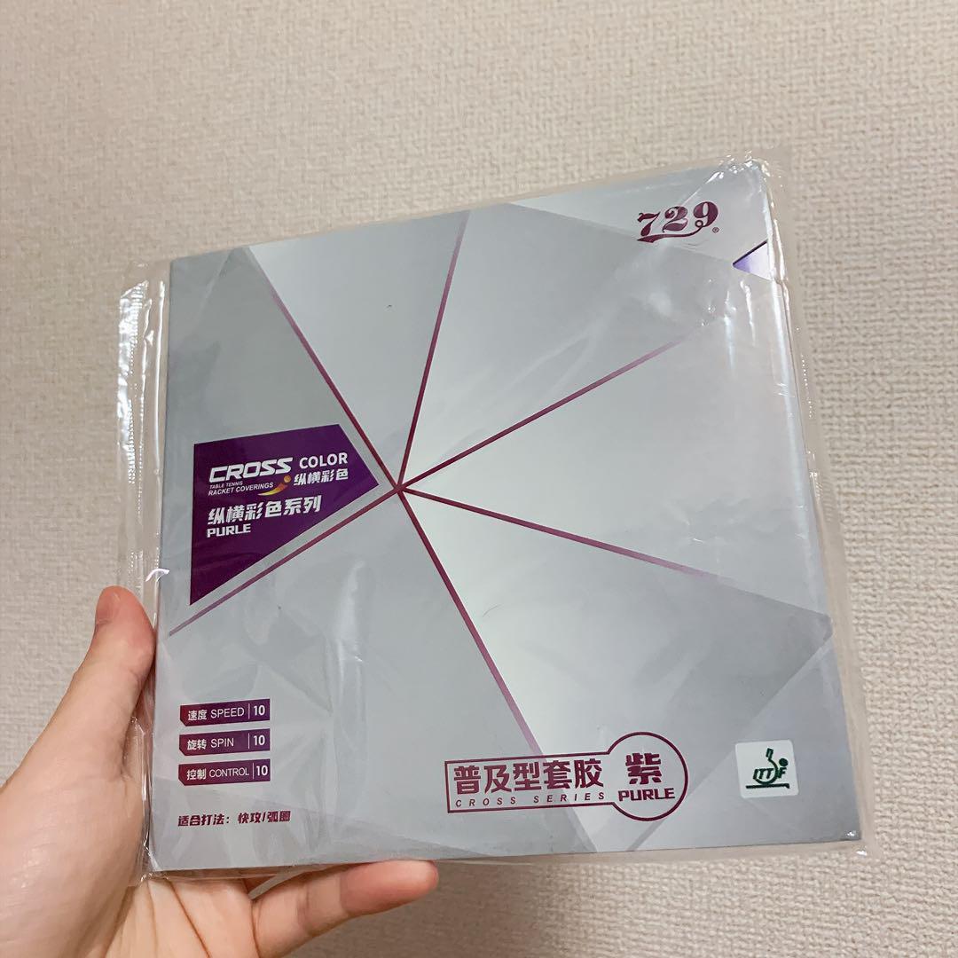 A hand holding sealed 729 packaged table tennis racket rubber showing the Cross Color series packaging and purple labeling.
