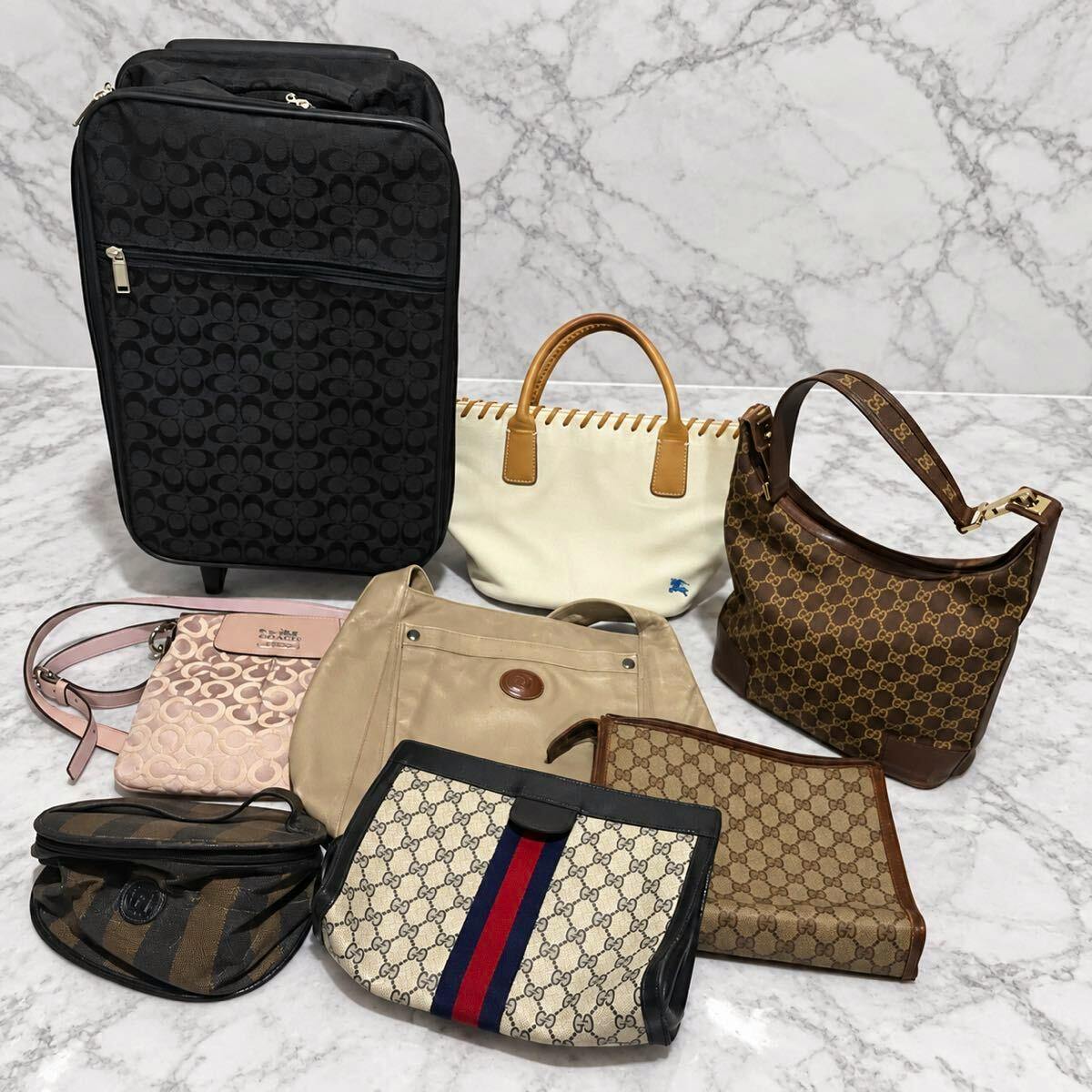 Eight designer bags and purses arranged on a marble surface, including a brown GG-pattern Gucci shoulder bag.