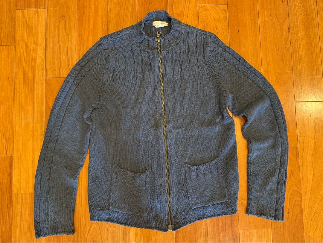 A Dries Van Noten zip-up knit sweater laid flat on a wooden floor.