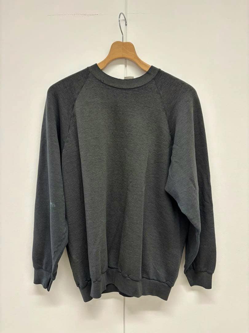 Dark gray cotton sweatshirt hanging on a wooden hanger against a white wall.