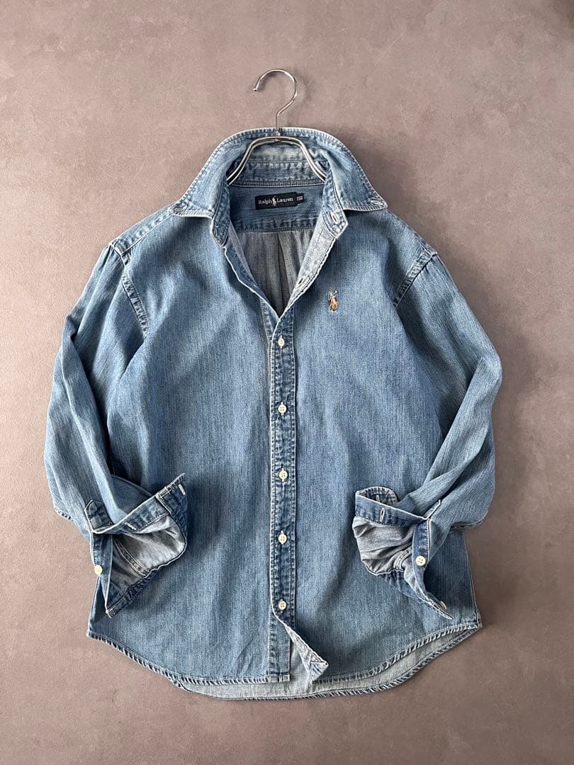 Light-blue Ralph Lauren denim women's shirt shown hanging on a hanger from the front with rolled sleeves and the embroidered pony logo on the chest.