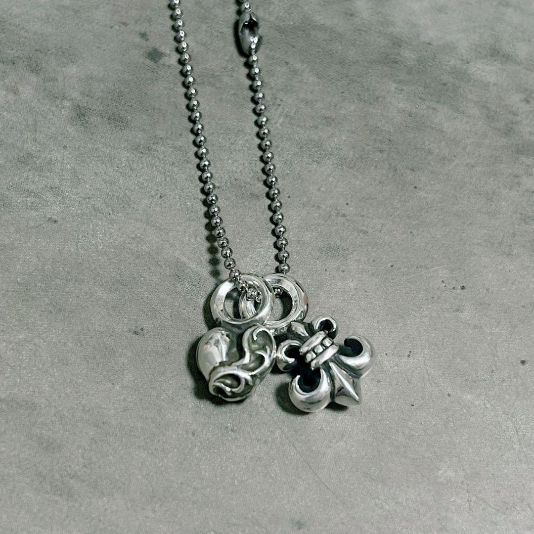 Silver heart and flared mini charm pendant on a ball chain necklace lying on a gray background.