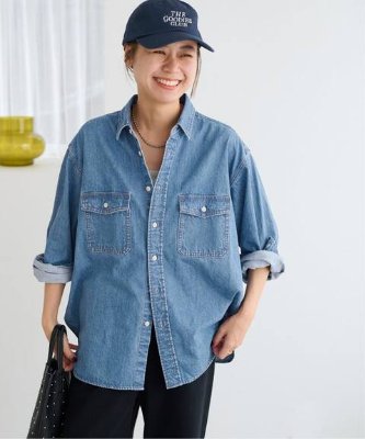 Female model wearing a light blue denim work shirt with two chest pockets and rolled sleeves.