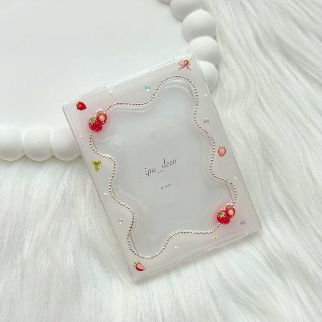Clear acrylic trading-card case decorated with strawberry stickers and bead-like rhinestones on a white fur surface.