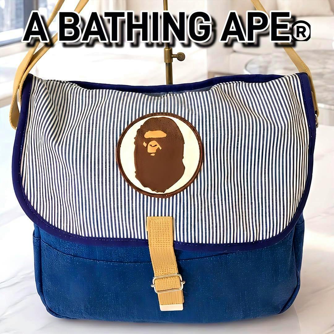 Front view of a denim canvas A BATHING APE shoulder bag with a striped flap and ape-head logo patch.