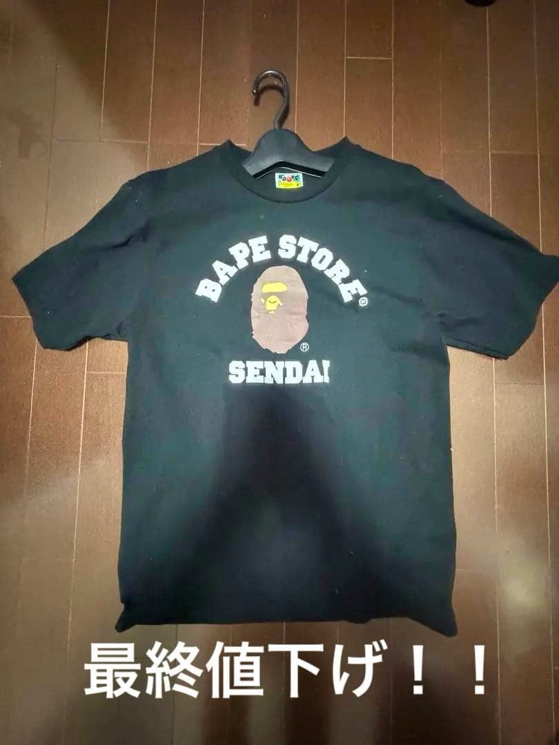 Front view of the A BATHING APE BAPE STORE SENDAI men's cotton T-shirt on a hanger showing the front logo on a wooden floor.