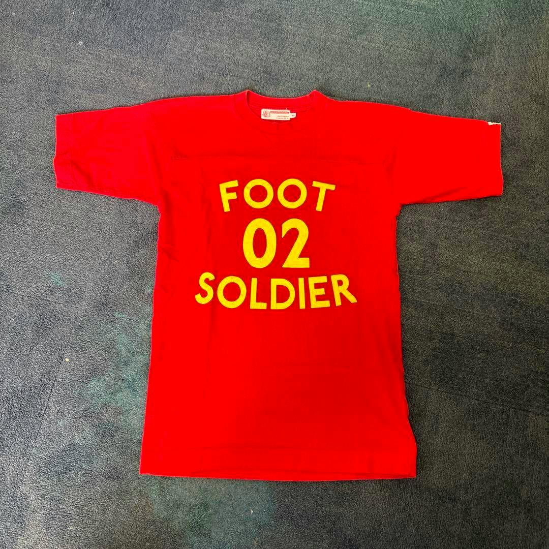 Red A BATHING APE T-shirt laid flat showing the front with yellow “FOOT 02 SOLDIER” text.