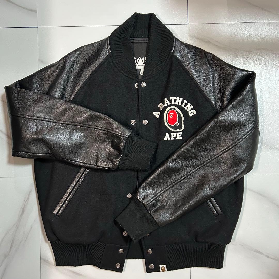 Front view of a black A Bathing Ape varsity jacket with leather sleeves and a chest logo patch.