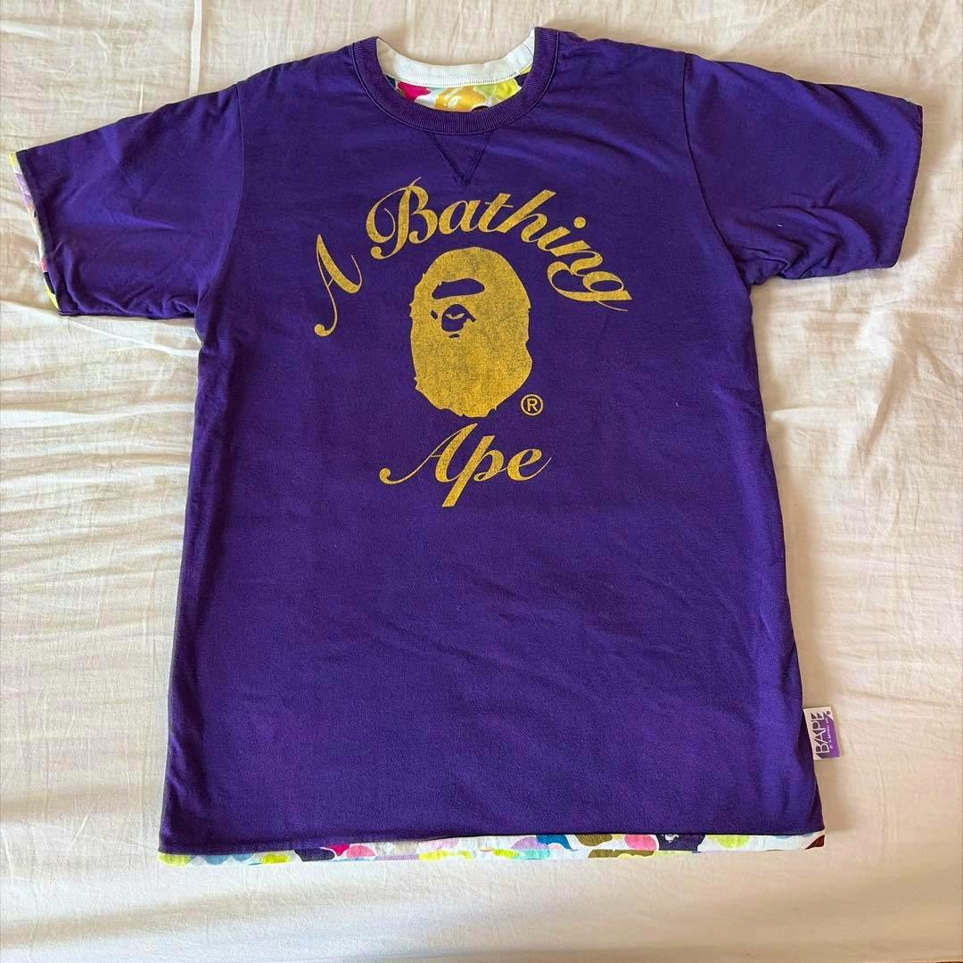 Front of a purple A Bathing Ape reversible T-shirt laid flat with a gold ape head logo and "A Bathing Ape" text.