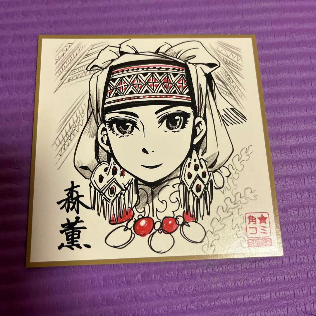 Mini picture board (shikishi) showing a printed illustration from 乙嫁語り by 森薫 of a woman's face in traditional headwear with a printed signature and publisher stamp on a purple textured surface.
