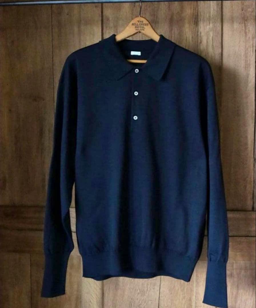 Dark navy long-sleeve cotton knit polo shirt hanging on a wooden hanger against a wood background.