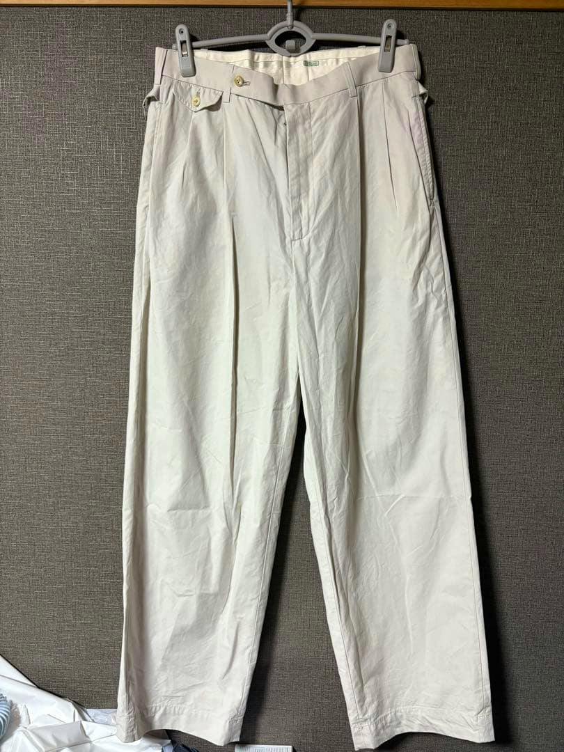 Front view of the アプレッセ High Density Weather Trousers (men's polyester pants) hanging on a hanger against a wall.