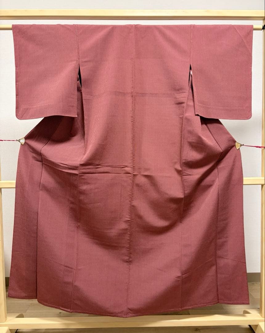 Front view of a women's azuki-colored silk kimono with subtle vertical stripes displayed on a wooden kimono stand.