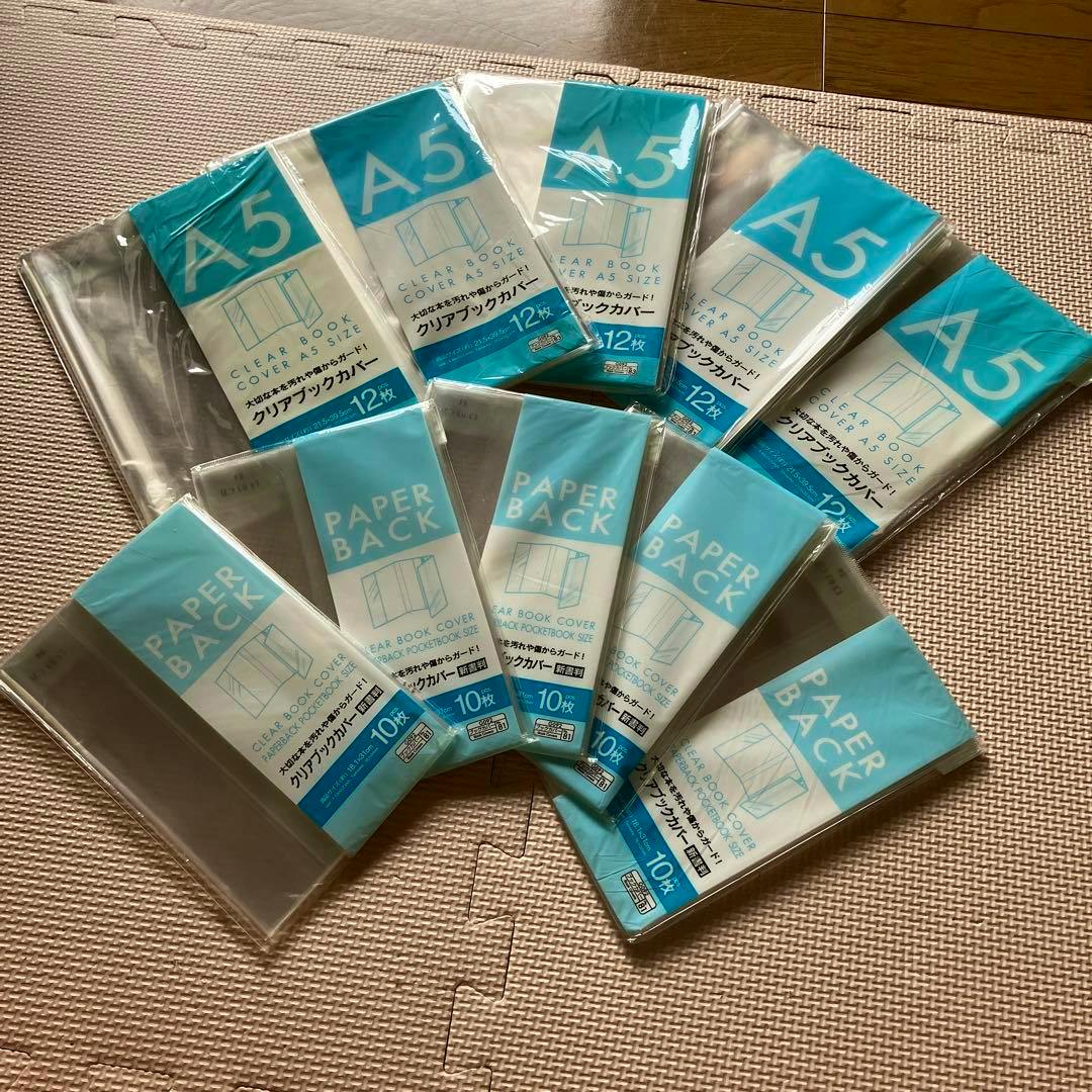 Multiple packs of A5 clear book covers and paperback covers in plastic packaging arranged on a mat.