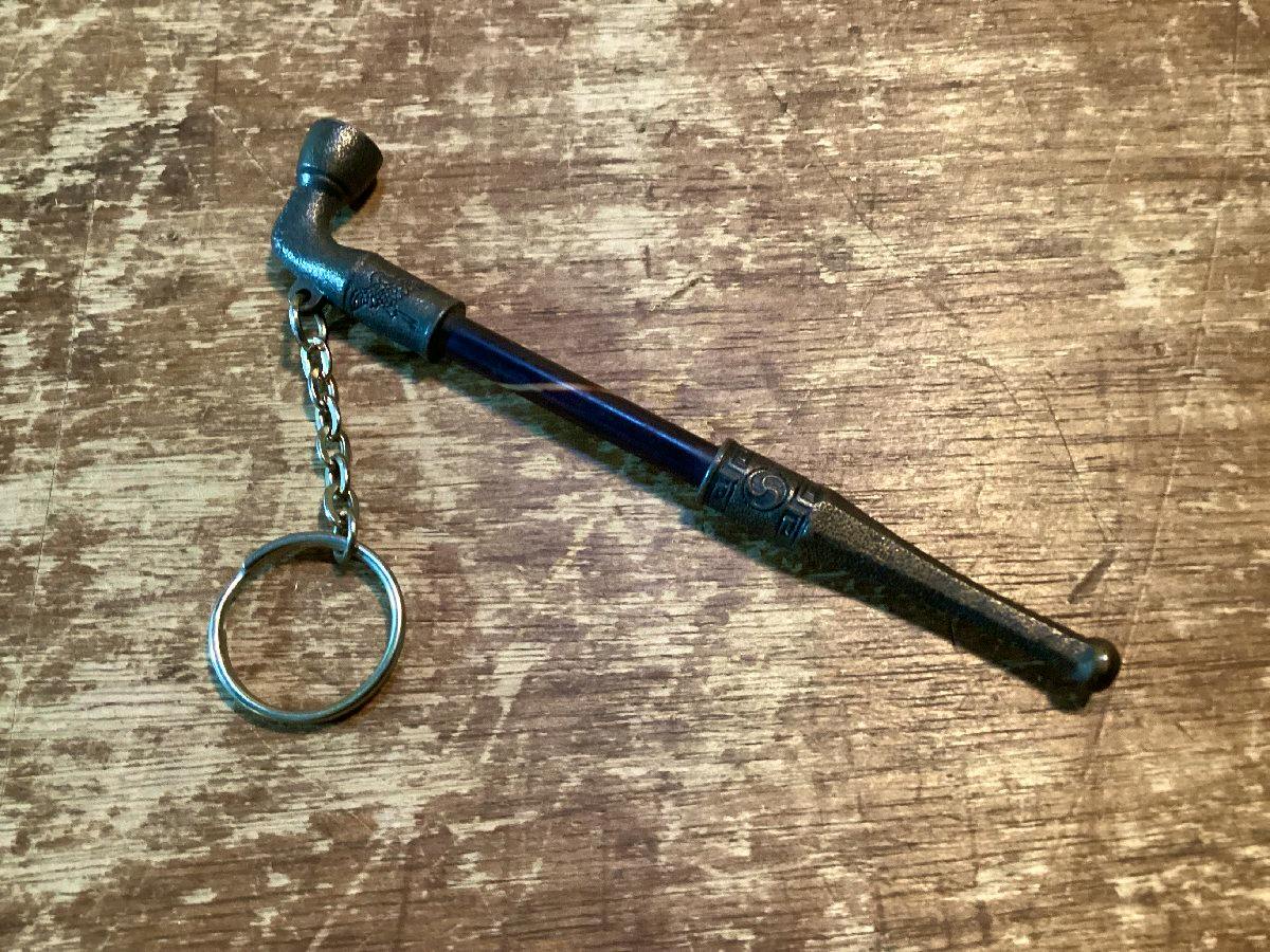 A pipe-shaped keychain with a short chain and split ring placed on a wooden surface.