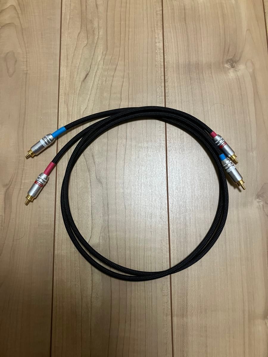 RCA cable with braided black jacket and gold-plated RCA plugs coiled on a wooden floor.
