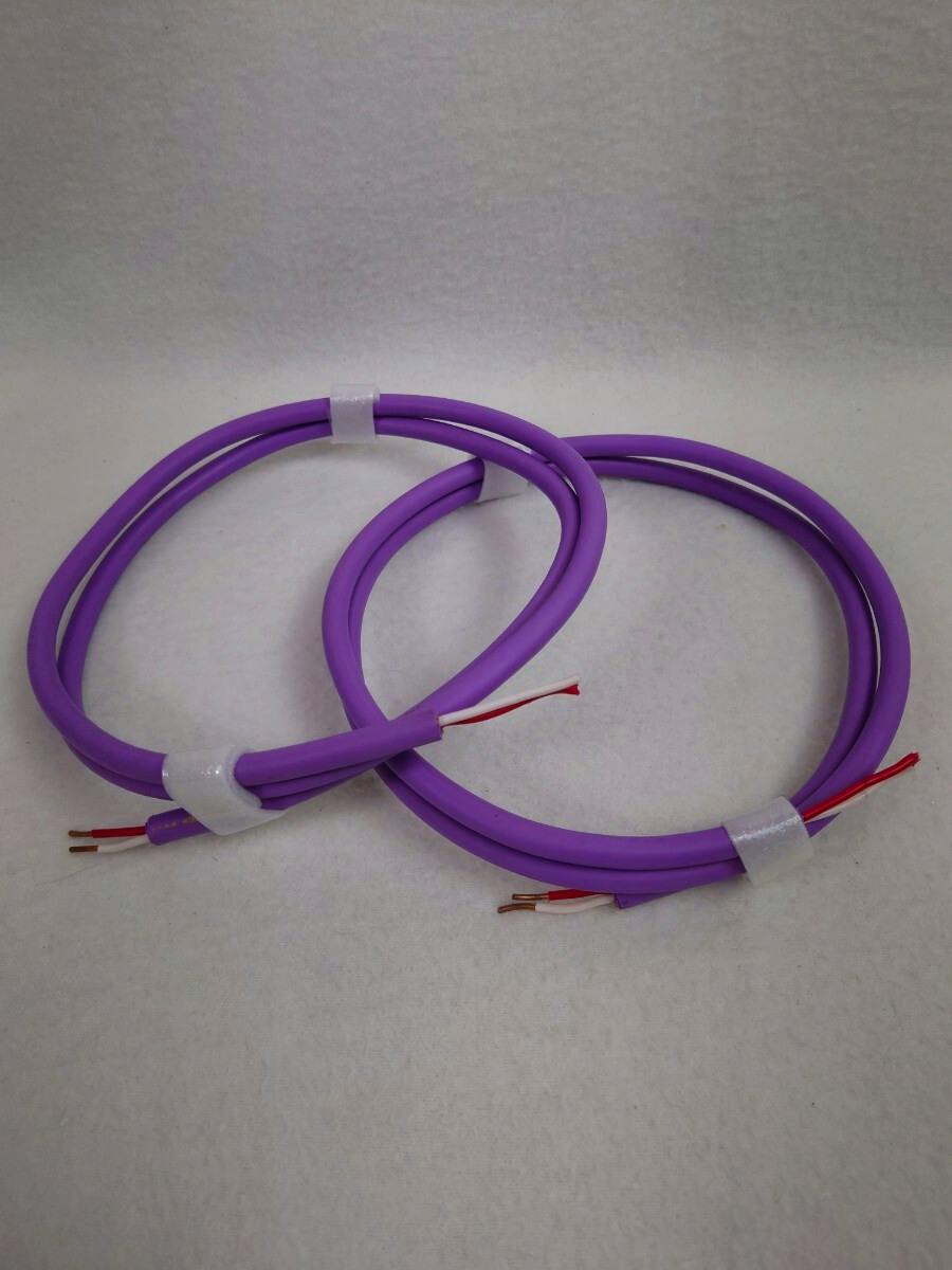 Coiled pair of purple speaker cables with exposed bare wire ends on a white background.