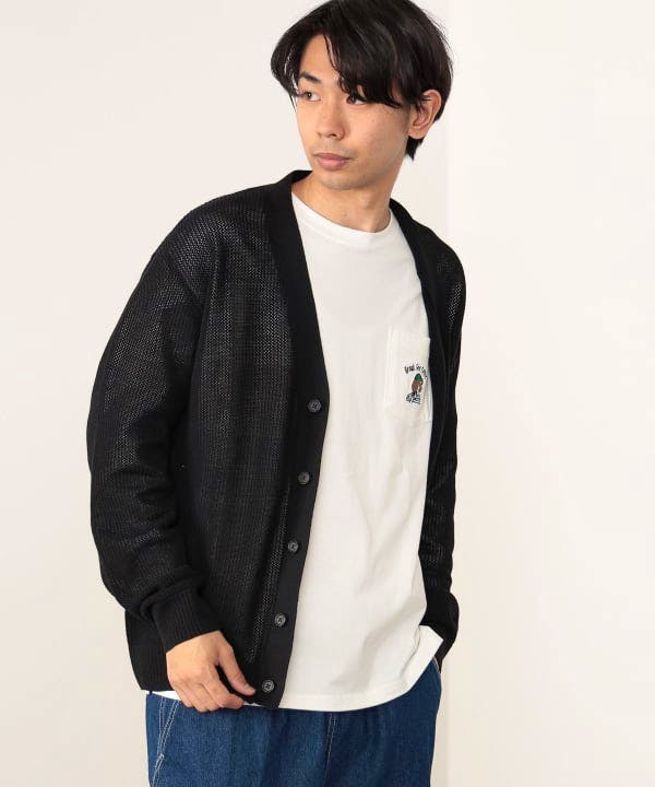 Male model wearing a black acrylic knit cardigan over a white T-shirt and blue pants.