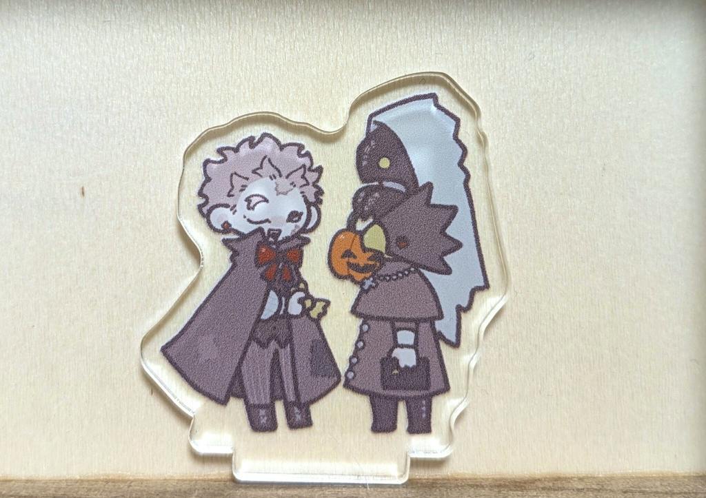 A clear acrylic decorative stand showing two stylized characters, one holding a small pumpkin, on a light background.