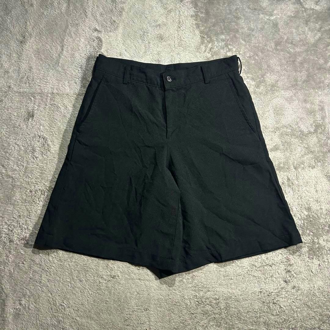 Black men's wide shorts laid flat on a light gray textured surface showing the front.