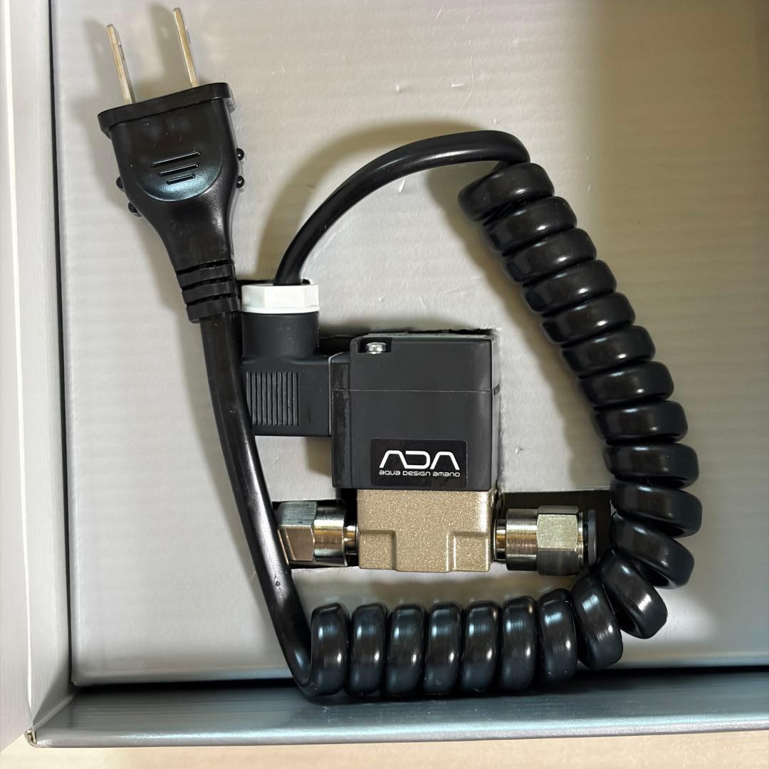 Close-up of an ADA EL-valve electromagnetic CO2 valve with coiled cord and power plug shown in its box.