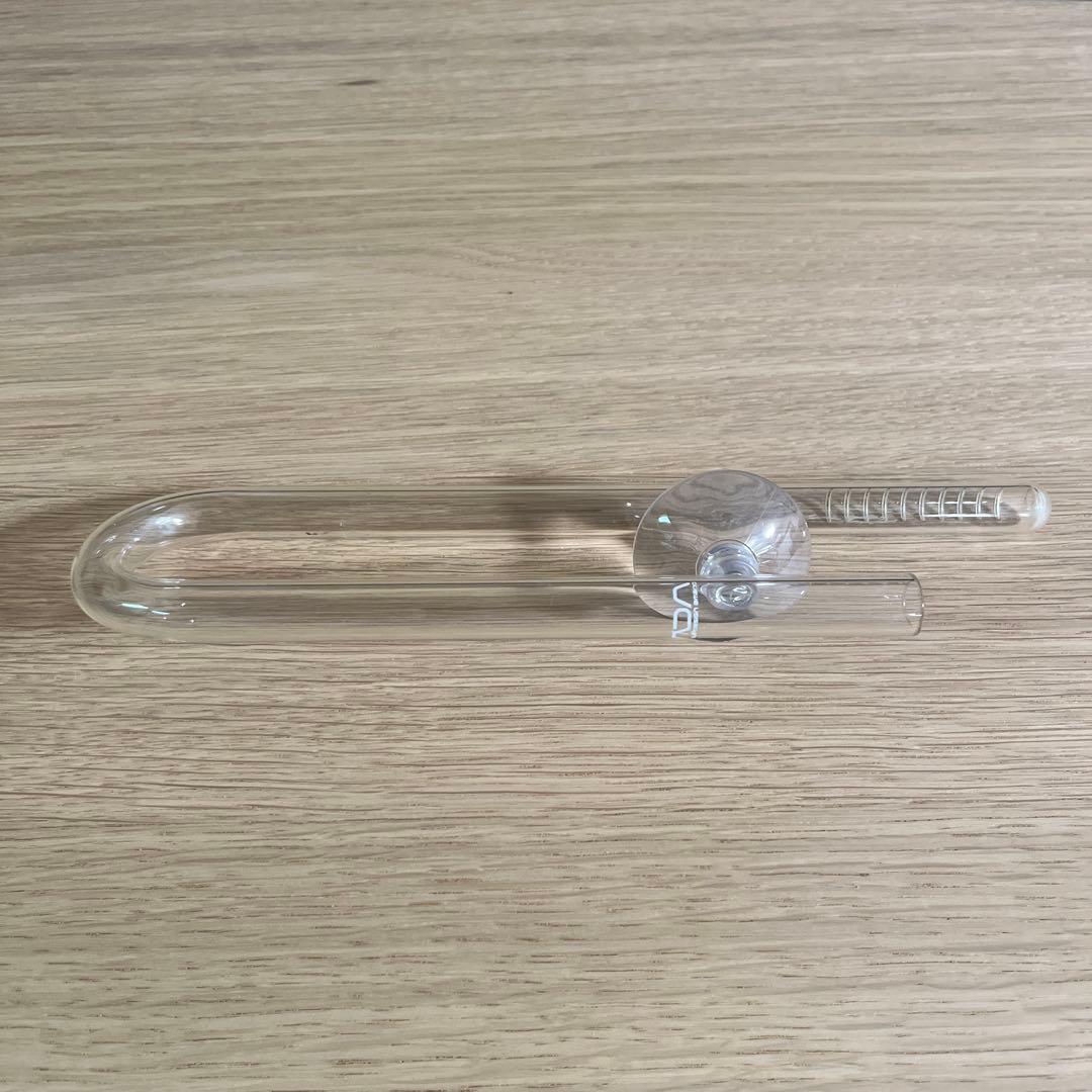 Glass ADA lily aquarium intake pipe laid on a wooden surface, showing the curved outlet and attached suction cup.