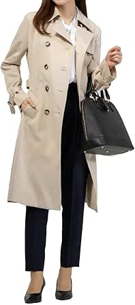 Model wearing a beige women's long trench coat over a white blouse and black trousers while holding a black handbag.